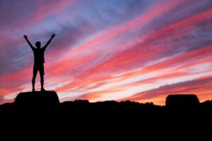 silhouette of a man standing on elevated ground beneath red and blue skies